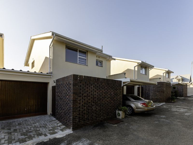 Front elevation of a townhouse complex featuring brick boundary walls, a paved driveway, a garage, and a covered carport area.