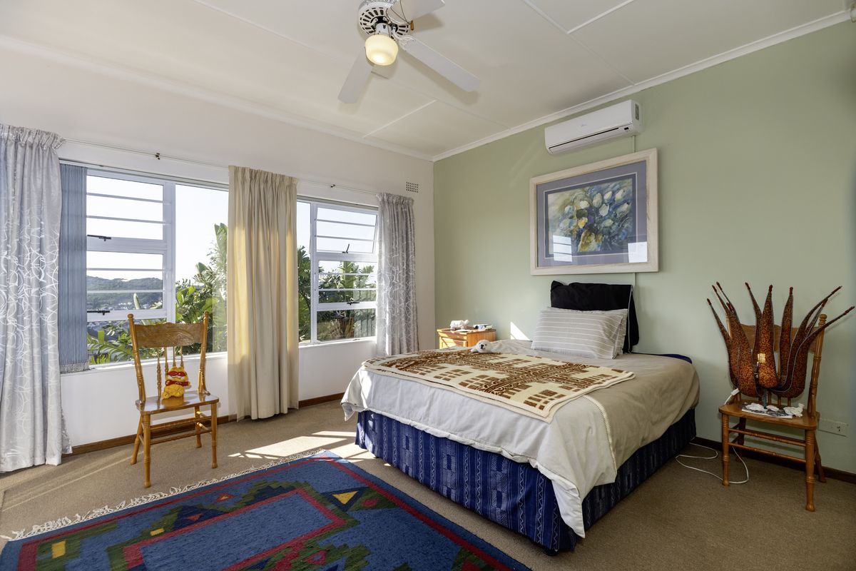 A well-lit bedroom featuring a ceiling fan, split-system air conditioning, and large windows providing natural light and exterior views.