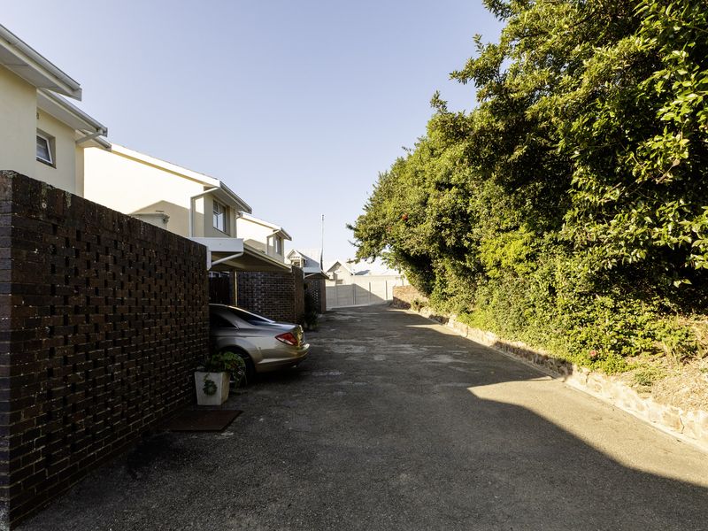 Exterior view of the townhouse complex driveway featuring brick boundary walls, a carport, and established garden landscaping along the side.