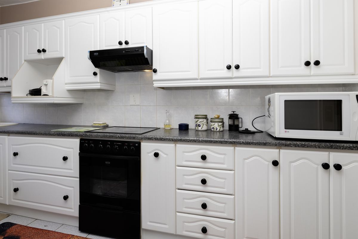 A functional kitchen featuring white cabinetry, dark laminate countertops, a built-in electric oven with hob, and a tiled backsplash.