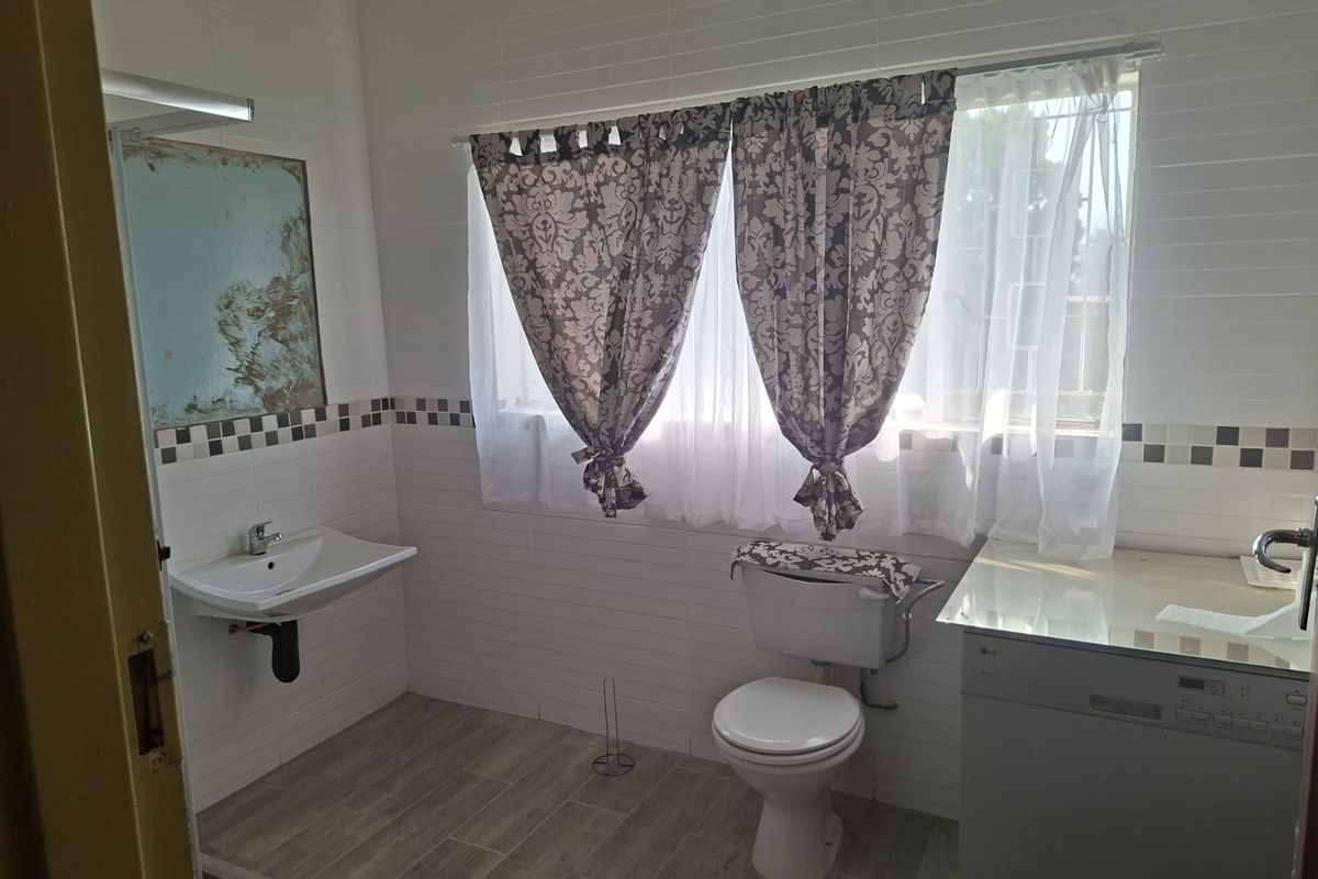 A functional bathroom featuring a wall-mounted basin, toilet, and tiled finishes, with a window providing natural light.