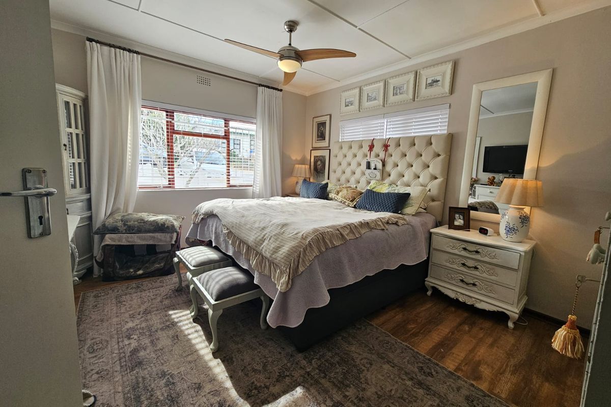 A well-lit bedroom featuring wood-look flooring, a ceiling fan, and large windows that provide natural light.