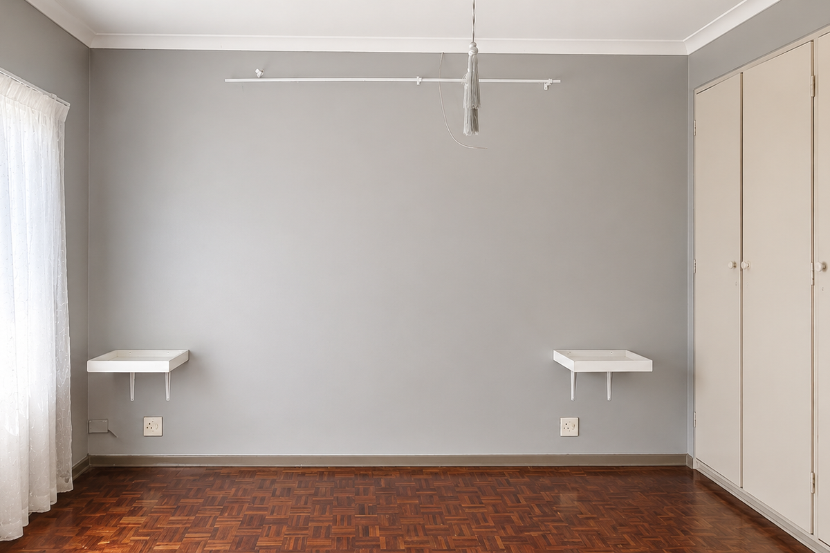 A bright, empty bedroom featuring original parquet flooring, built-in cupboards, and wall-mounted bedside shelving.