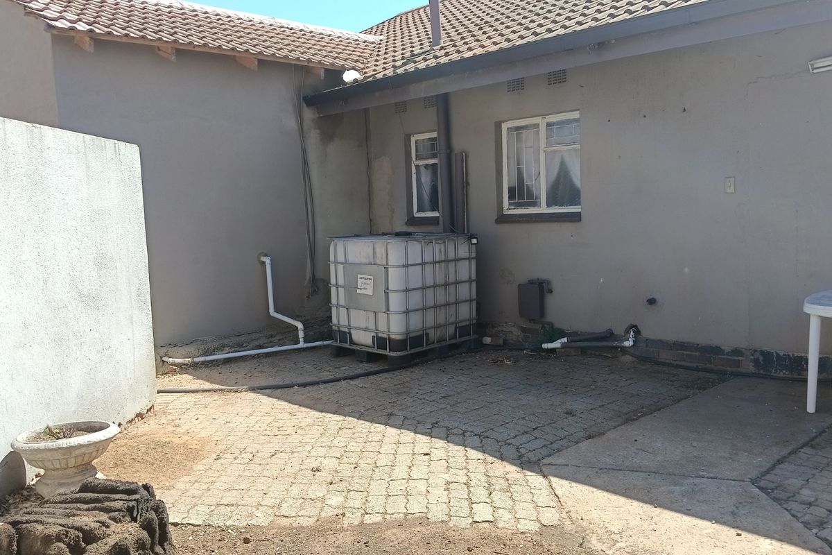Rear exterior area featuring paved ground, a water storage tank, and exposed exterior wall surfaces with basic window fixtures.