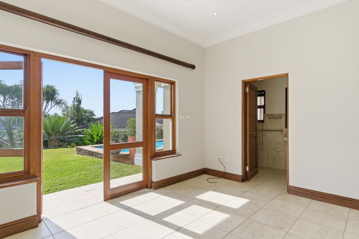 Bright bedroom featuring tiled flooring, timber-framed glass sliding doors opening to the garden, and an en-suite bathroom.