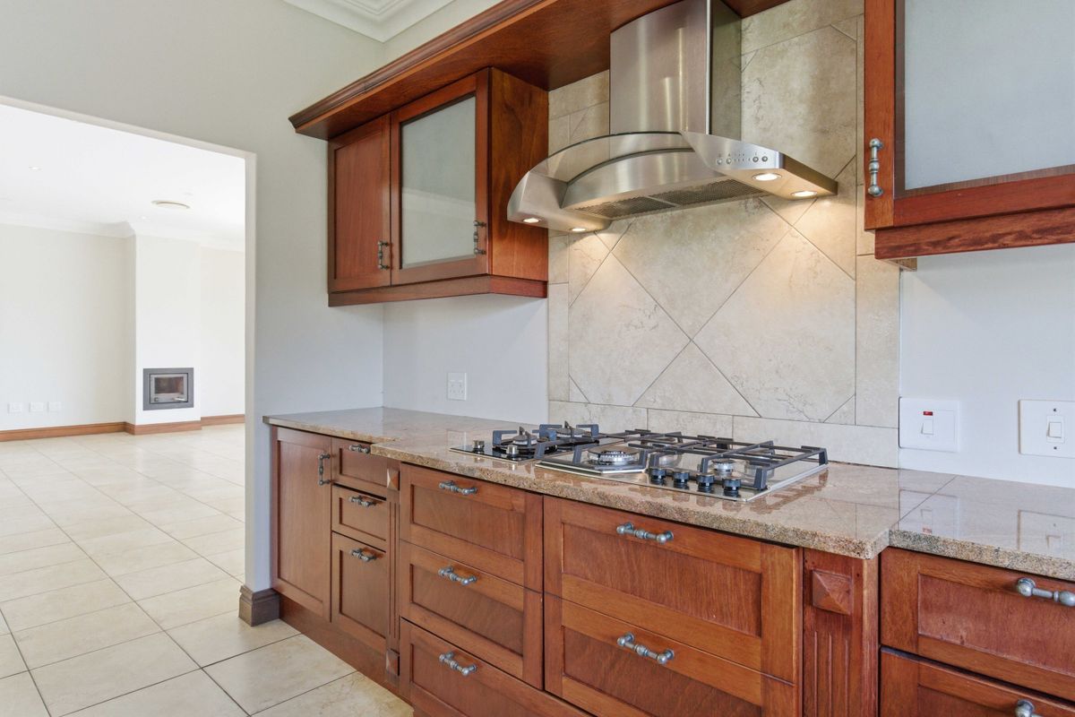 A well-maintained kitchen featuring rich timber cabinetry, granite countertops, a built-in gas hob, and a stainless steel extractor fan.