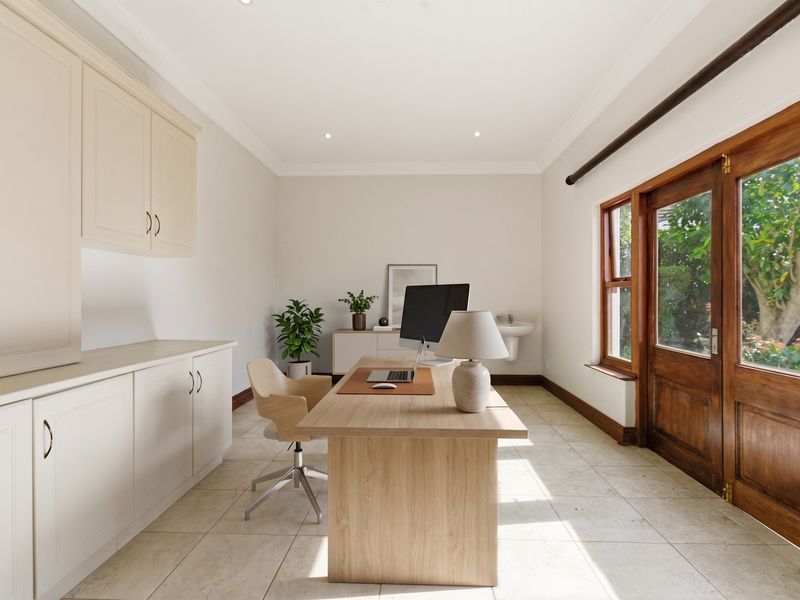 A bright home office featuring built-in cabinetry, tiled flooring, and direct access to the garden through timber-framed glass doors.