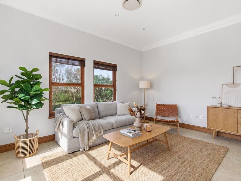 A bright and well-maintained living room featuring tiled flooring, timber-framed windows, and recessed downlighting, creating a clean and inviting atmosphere.