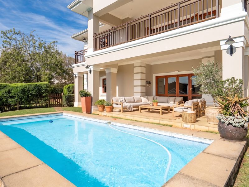 A well-maintained outdoor area featuring a swimming pool with stone coping, adjacent to a covered patio and an upper-level balcony with timber railings.