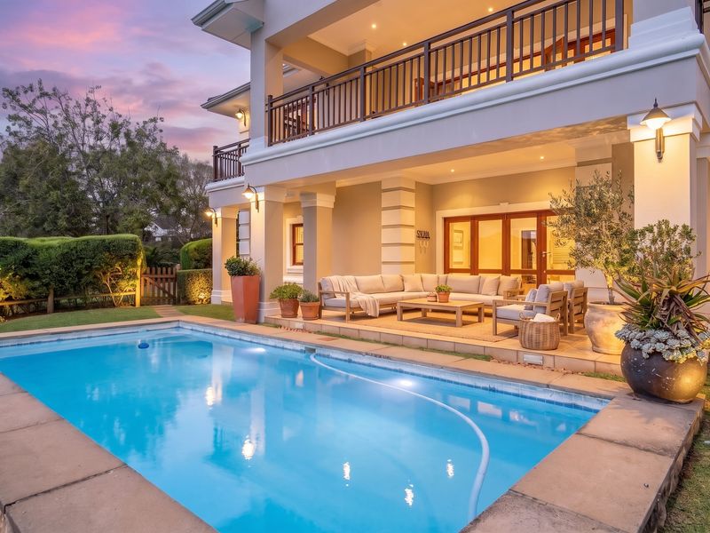 A beautifully maintained outdoor pool area featuring a tiled patio, upper-level balcony, and integrated exterior lighting, perfect for evening relaxation and entertainment.