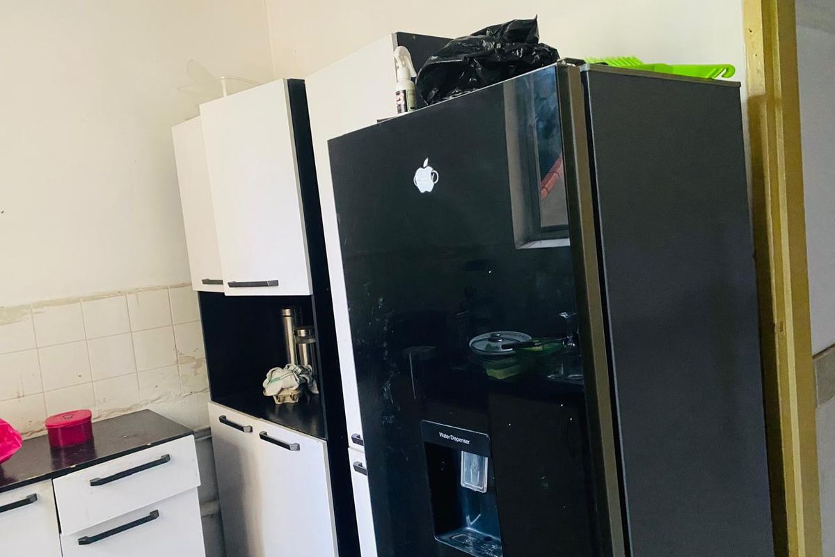 A kitchen area featuring white and black cabinetry with a built-in look, tiled splashback, and space for a large refrigerator.