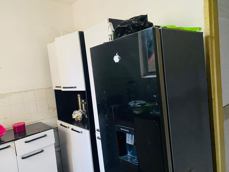 A kitchen area featuring white and black cabinetry with a built-in look, tiled splashback, and space for a large refrigerator.