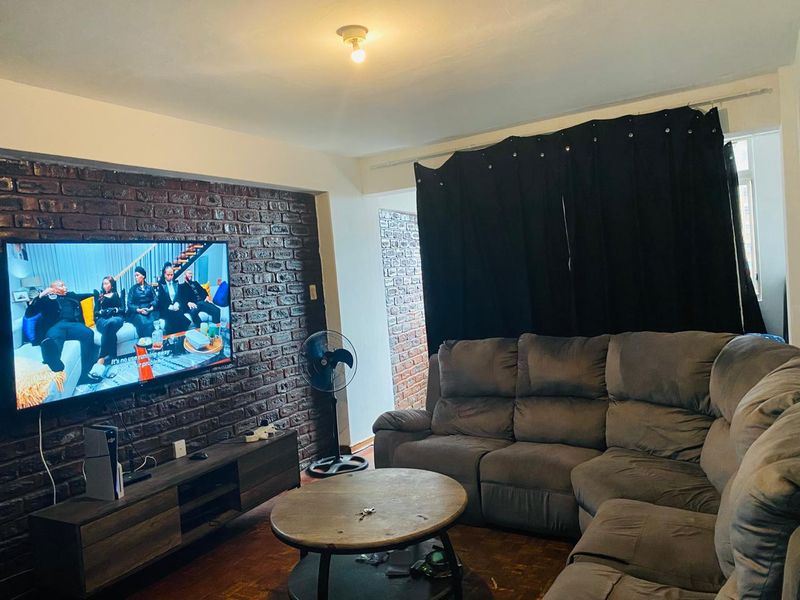 Living room featuring a prominent exposed brick feature wall, parquet flooring, and large window with curtain track.