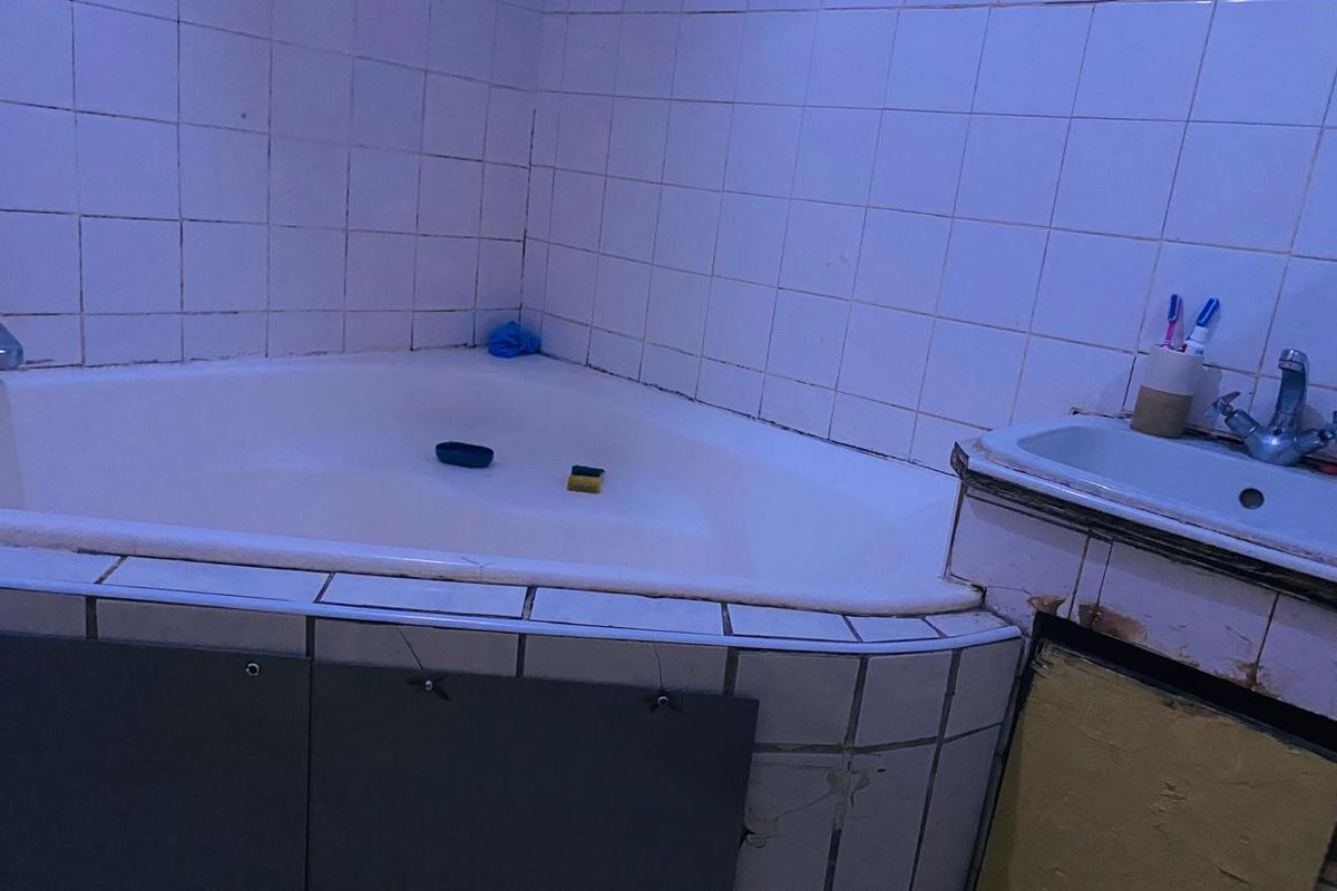 A dated bathroom featuring a corner bathtub and a vanity unit with visible wear and tear on the cabinetry and tiling.