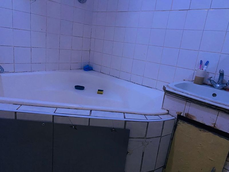 A dated bathroom featuring a corner bathtub and a vanity unit with visible wear and tear on the cabinetry and tiling.