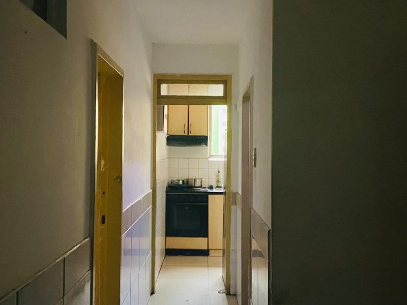 A narrow hallway leading into a compact kitchen area featuring built-in cabinetry, a stove, and an extractor fan.