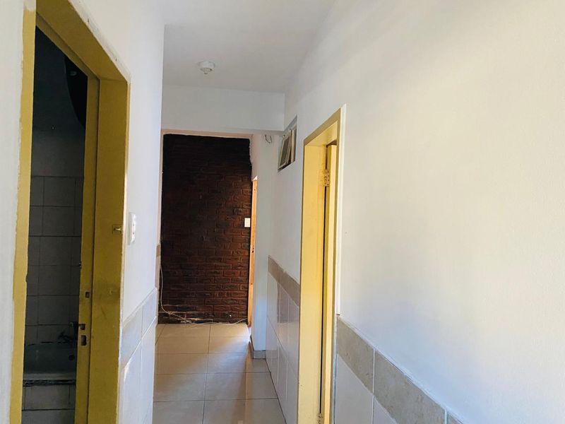 A vacant hallway featuring tiled flooring, partial wall tiling, and an exposed brick feature wall, leading to adjacent rooms.