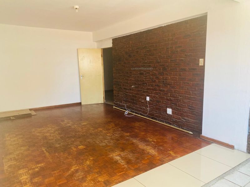An empty living room featuring a prominent exposed brick accent wall and a combination of parquet and tiled flooring, offering a blank canvas for renovation.