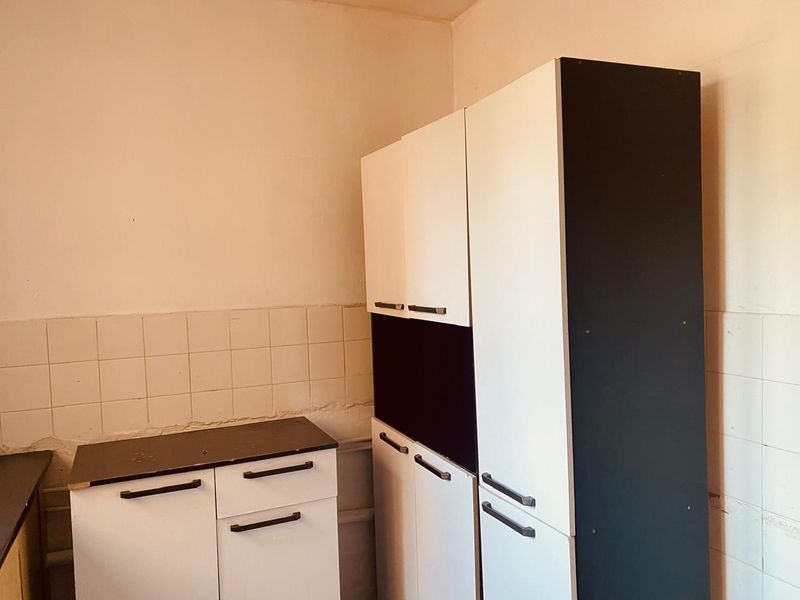 A compact kitchen area featuring built-in cabinetry with a two-tone finish and a tiled splashback, requiring some cosmetic attention to the surrounding wall surfaces.