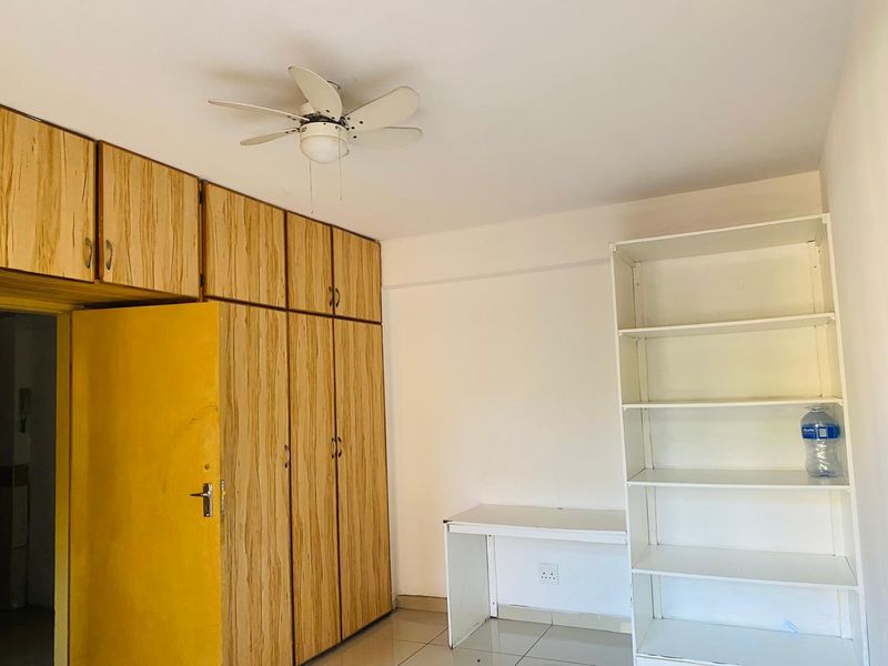 A bedroom featuring built-in wooden cupboards, a ceiling fan, tiled flooring, and a built-in desk with shelving.