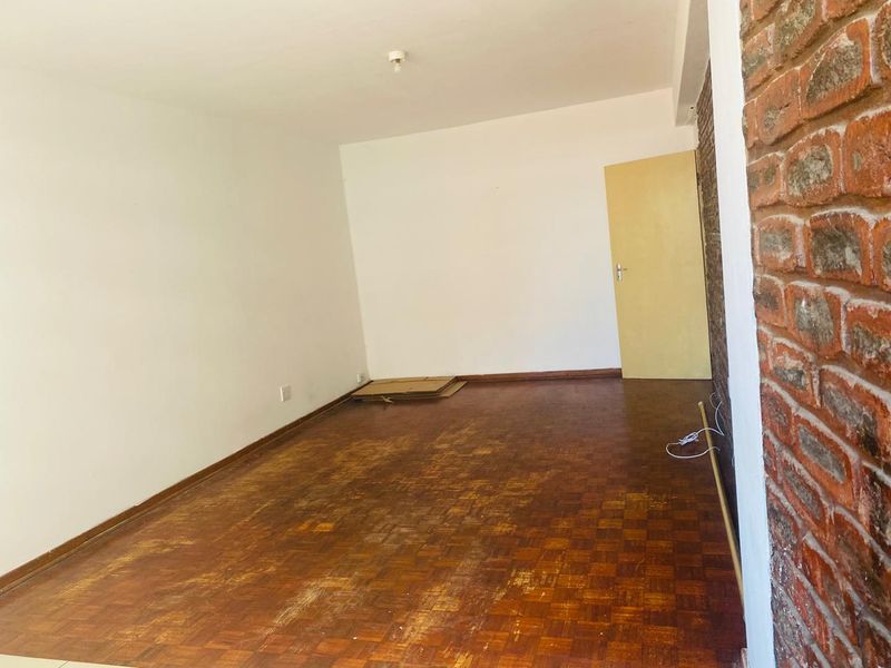 An empty living room featuring original parquet flooring and an exposed brick feature wall, offering a blank canvas for renovation.