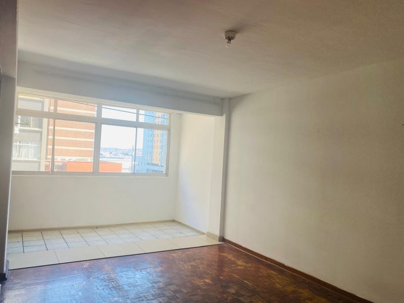 An empty living room featuring a combination of parquet and tiled flooring with a large window providing natural light.