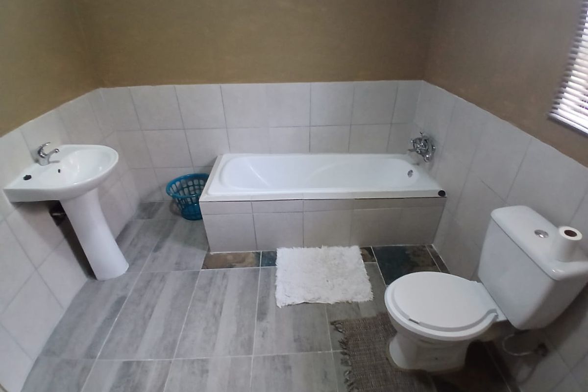 A functional bathroom featuring a white pedestal basin, a built-in bathtub with tiled surround, and a standard toilet.