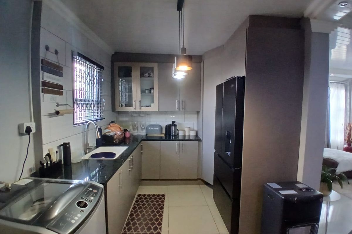 A functional kitchen featuring modern cabinetry, dark stone countertops, a stainless steel sink, and integrated lighting, seamlessly connected to the adjacent living area.