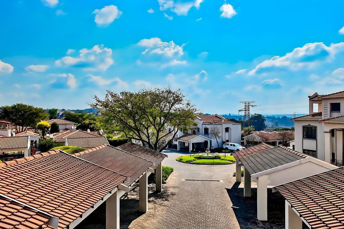 Elevated view overlooking a residential townhouse complex with paved driveways, tiled roofing, and a central landscaped roundabout.