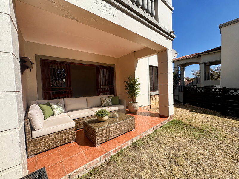 A covered patio area featuring tiled flooring and security gates, providing direct access to the rear garden space.