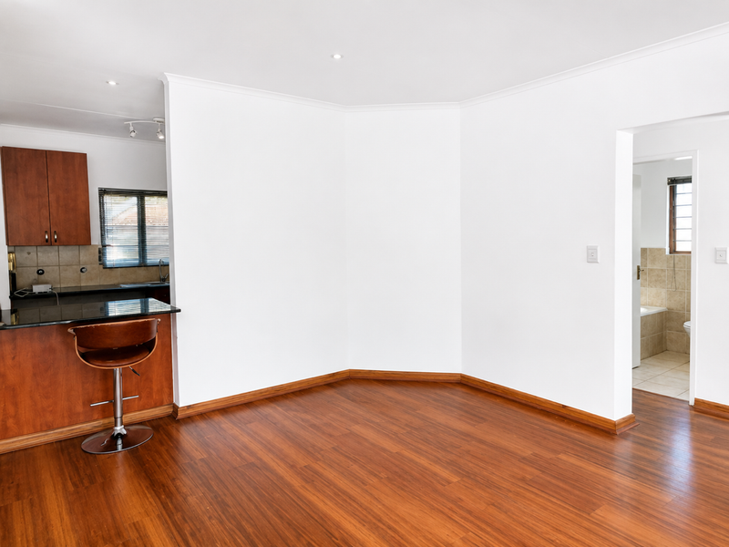 Open plan living area featuring warm-toned laminate flooring, a compact kitchen with granite countertops, and direct access to an adjacent bathroom.