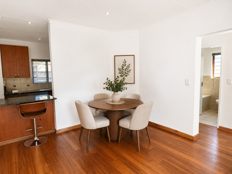 Open plan dining area featuring warm wooden flooring, adjacent to a kitchen with granite countertops and wooden cabinetry, with a view into a bathroom.