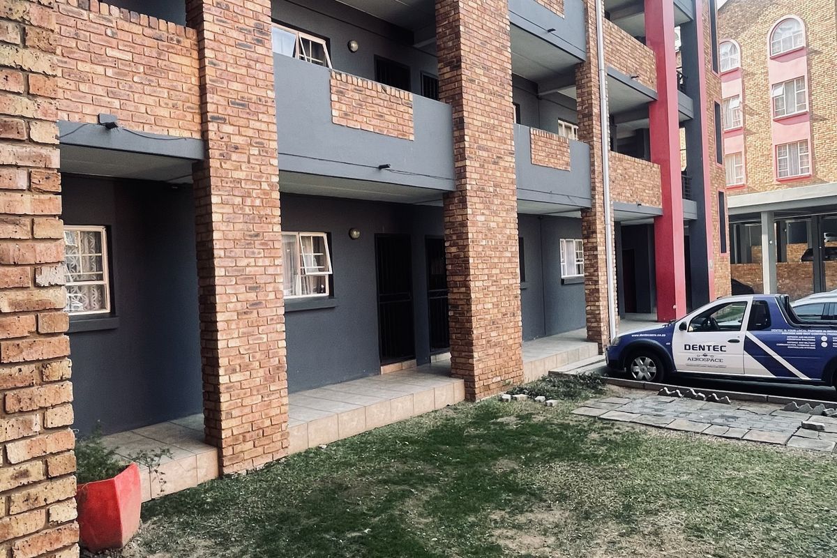 Exterior view of a multi-story apartment building featuring brick pillars, private balconies, and a ground-level tiled patio area.