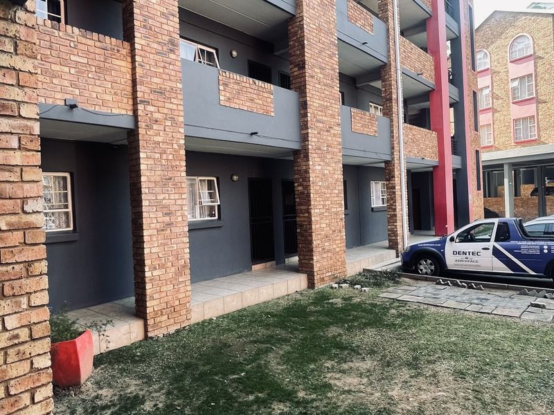 Exterior view of a multi-story apartment building featuring brick pillars, private balconies, and a ground-level tiled patio area.