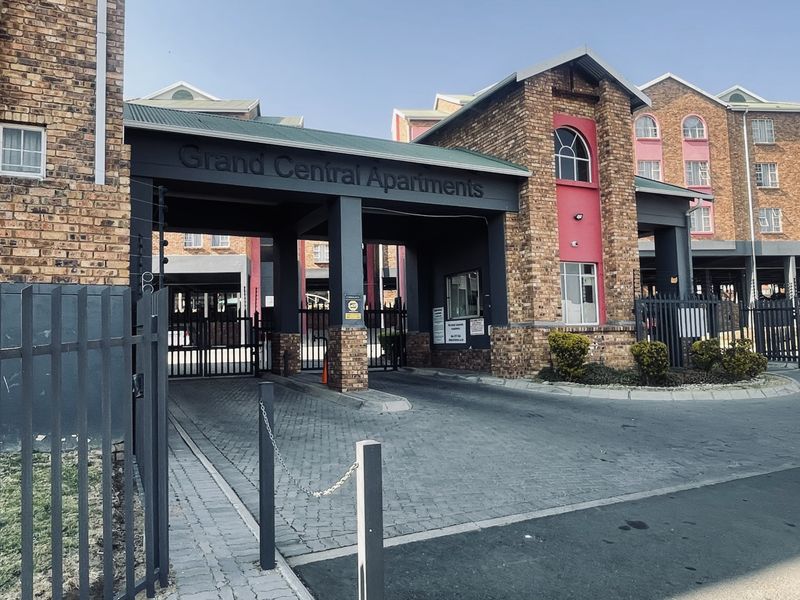 The entrance to Grand Central Apartments featuring a secure gated access point, brick facade architecture, and a paved driveway.