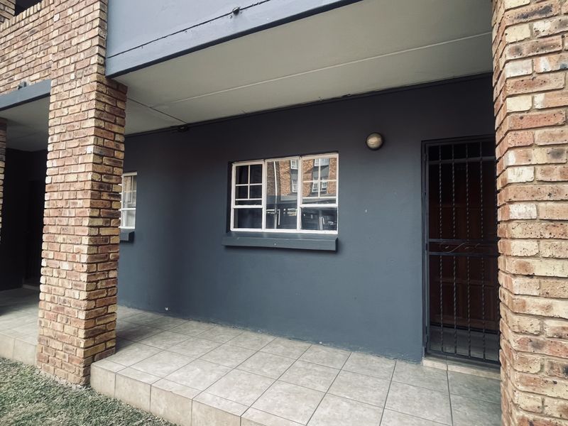 A covered patio area featuring tiled flooring, brick support pillars, and a secure entrance door with a metal security gate.