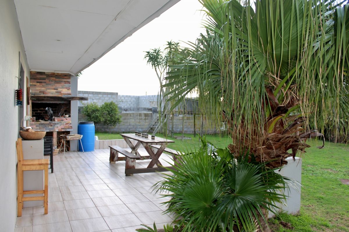 Covered patio area featuring a built-in brick braai, tiled flooring, and direct access to a garden space with established palm trees.