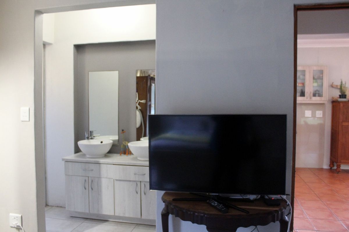 A view of a bathroom featuring a double vanity with vessel sinks and mirrors, adjacent to a living area with tiled flooring.