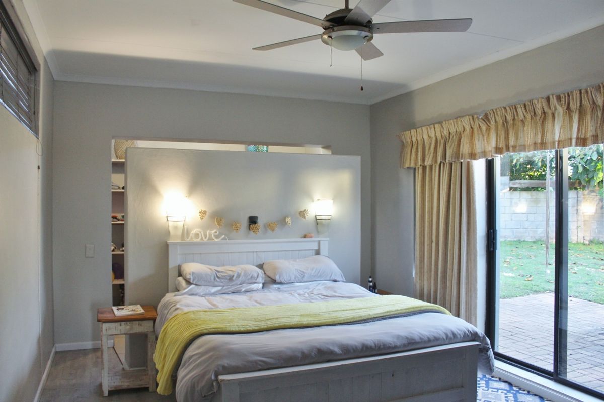 A bedroom featuring a built-in partition wall with integrated bedside lighting, a ceiling fan, and sliding glass doors providing access to the rear garden.