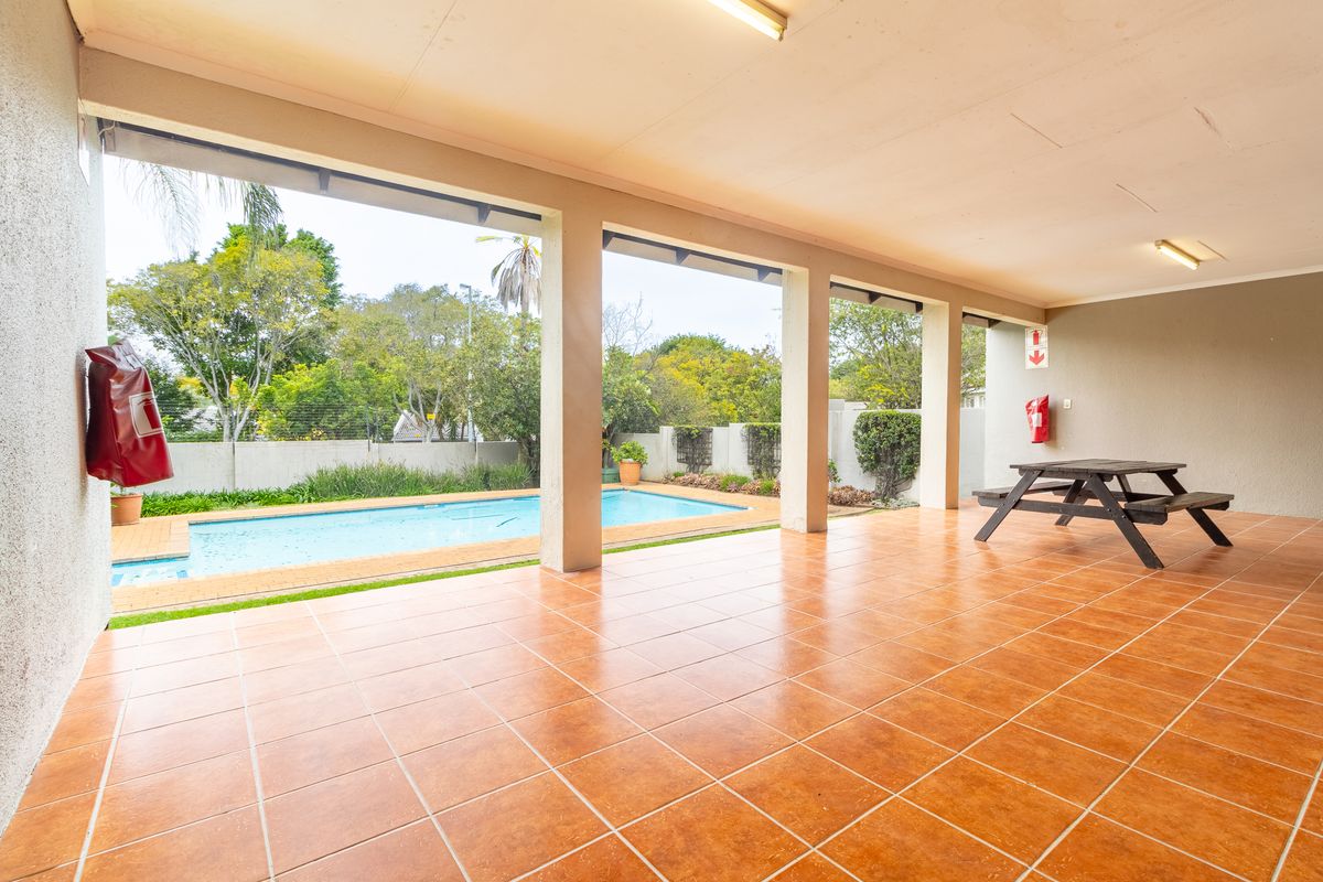 A spacious covered patio featuring terracotta-style floor tiles, overlooking a private swimming pool and garden area.