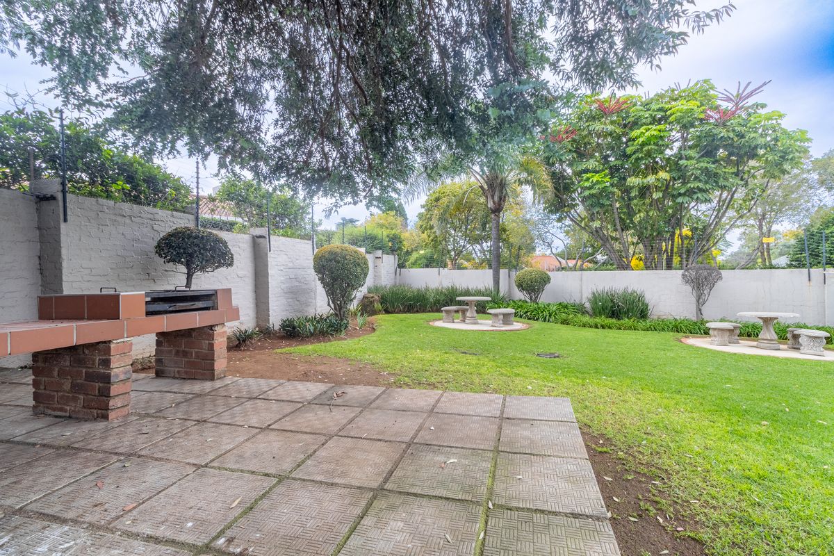 A private rear garden featuring a paved patio area with a built-in brick braai, lush lawn, and perimeter walling.