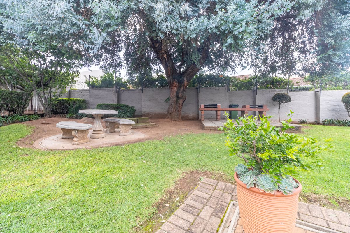 A private garden area featuring a built-in brick braai, paved seating area, and mature trees, providing a functional outdoor space for residents.