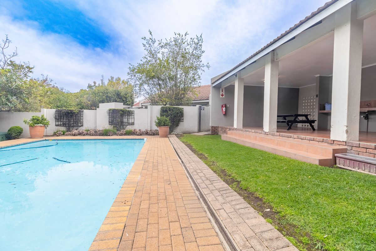 Outdoor entertainment area featuring a covered patio with built-in braai, overlooking a swimming pool and landscaped garden.
