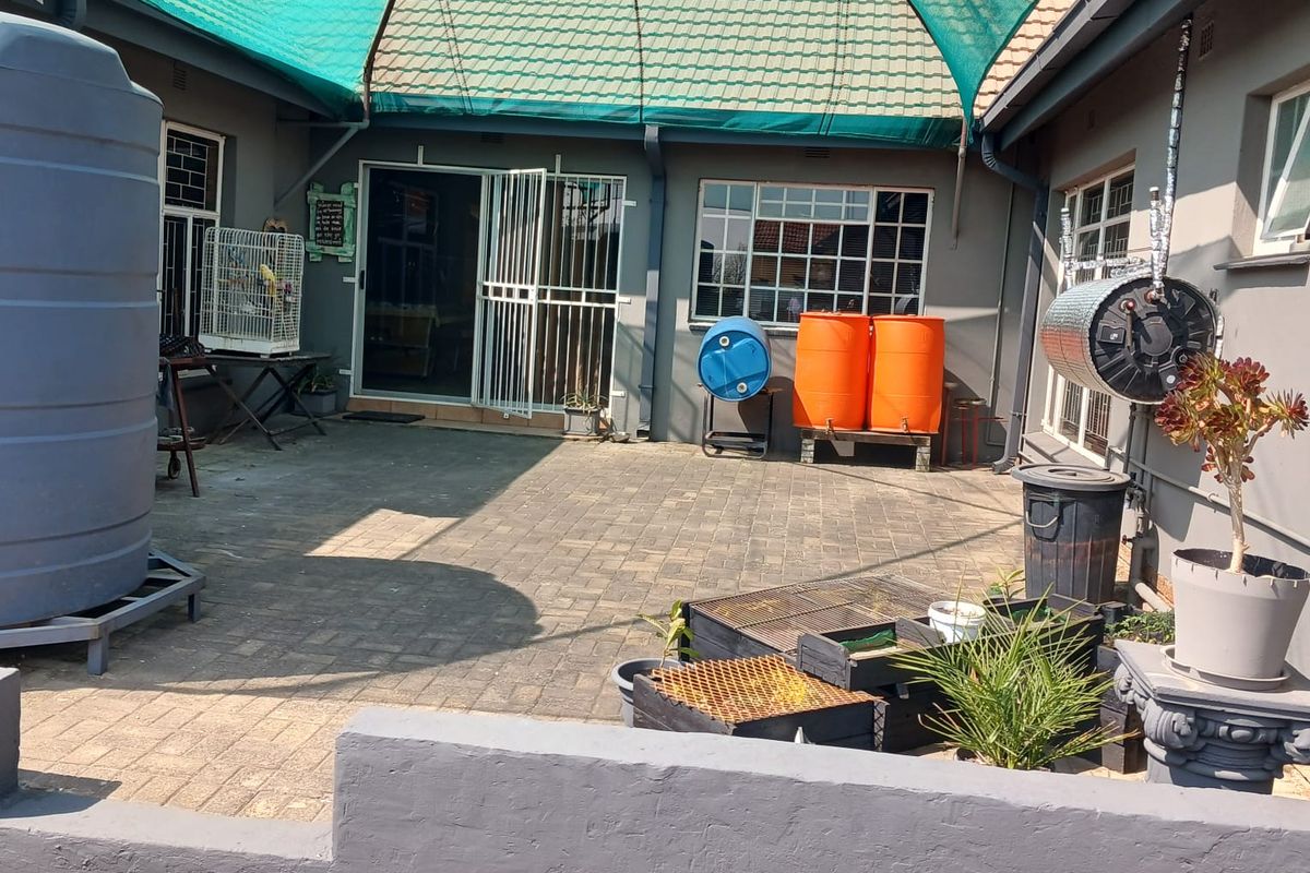 A paved rear courtyard area featuring a large water storage tank, shade netting, and security gates leading into the main dwelling.
