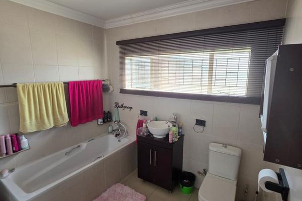 A functional bathroom featuring a built-in bathtub, a vanity cabinet with a vessel sink, a toilet, and tiled walls and flooring.