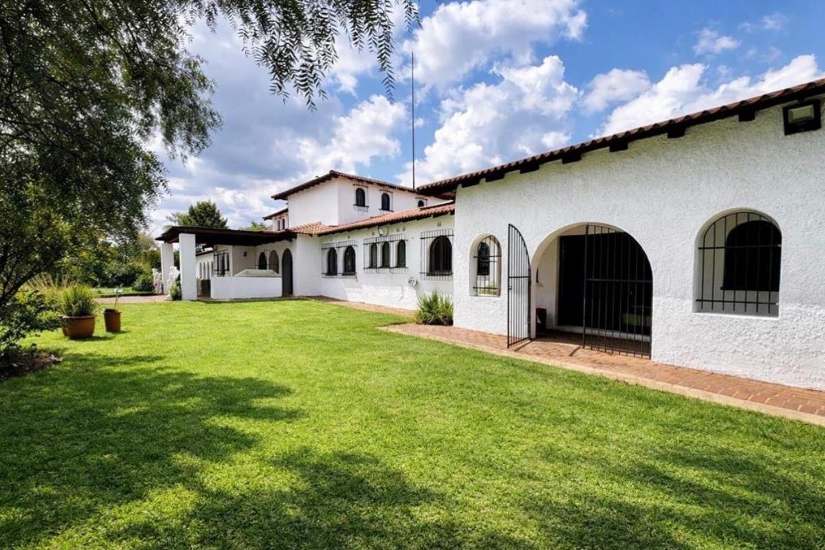A view of the rear exterior of the property, featuring white textured walls, arched doorways with security gates, and a well-maintained lawn.