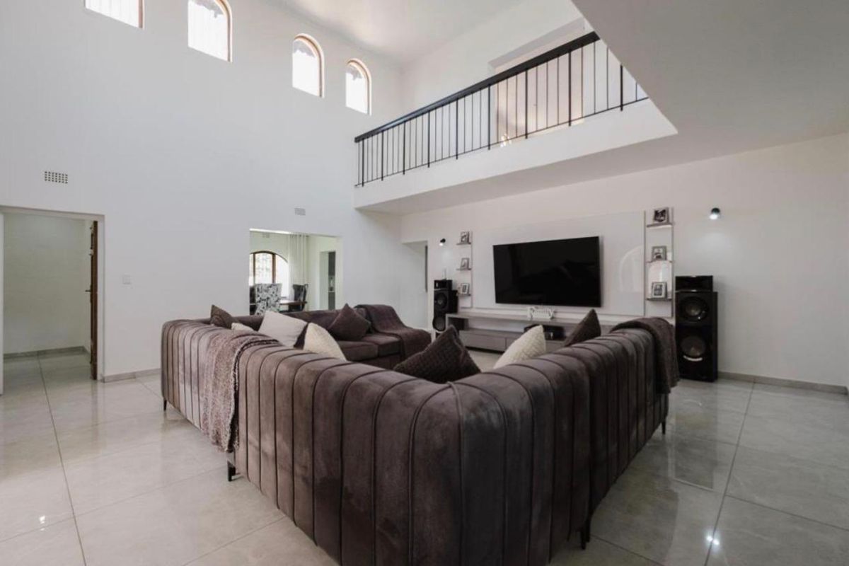 Spacious double-volume living area featuring a mezzanine balcony, tiled flooring, and built-in media wall cabinetry.