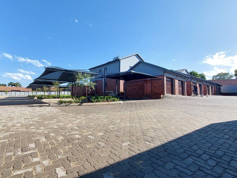 Exterior view of a townhouse complex featuring a paved driveway, multiple garage units, and covered shade cloth parking bays.