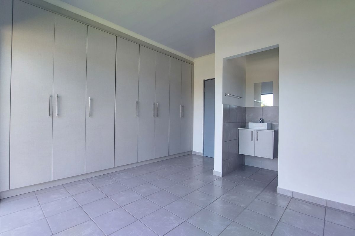 Spacious bedroom featuring extensive built-in cupboards, neutral tiled flooring, and an integrated vanity area with a modern basin.