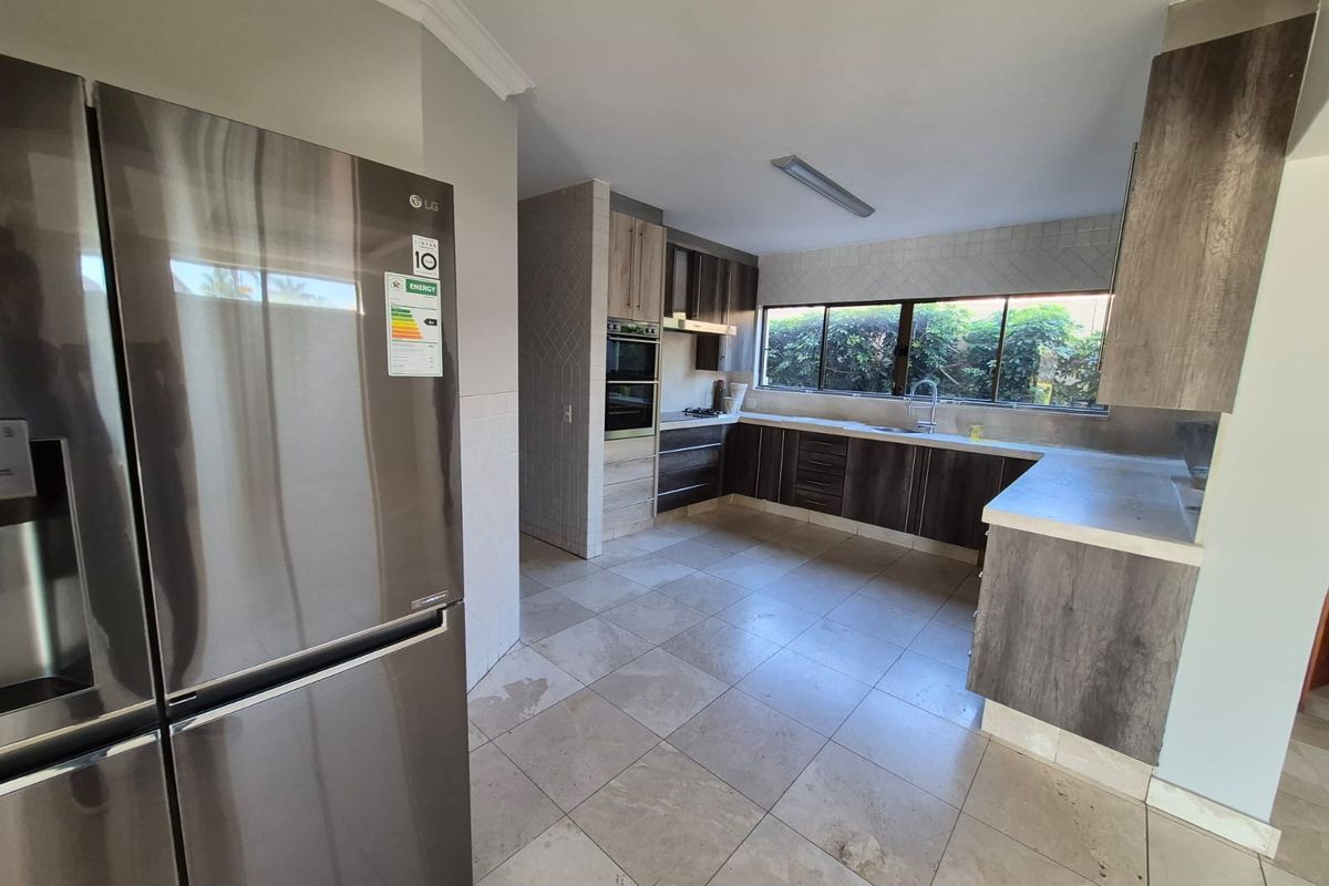 Modern kitchen featuring dark wood cabinetry, stone countertops, built-in oven, and large windows overlooking the garden.